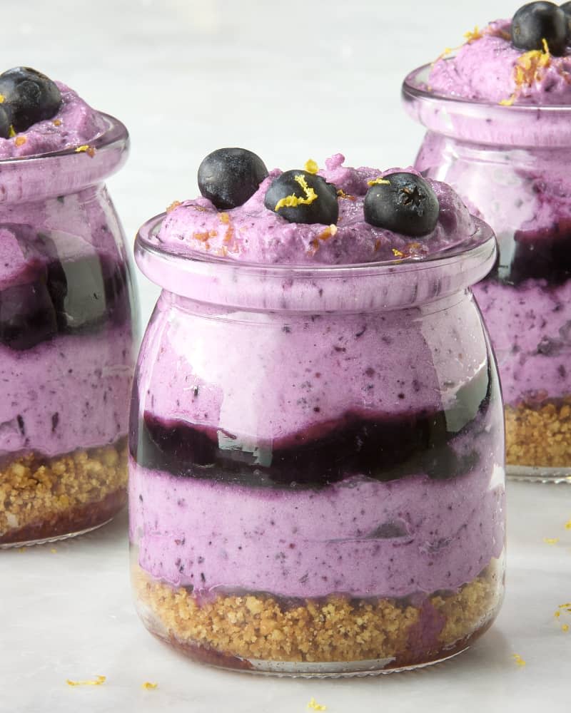 close up shot of three small jars of blueberry mousse, topped with lemon zest and small blueberries