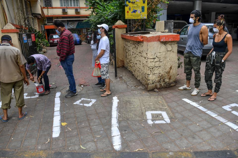 Customers watch municipal workers (L) painting white marks on the floor to help maintaining recommended social distanciation as they queue outside a departmental store during a government-imposed nationwide lockdown as a preventive measure against the COVID-19 coronavirus in Mumbai on March 26, 2020. (Photo by INDRANIL MUKHERJEE / AFP) (Photo by INDRANIL MUKHERJEE/AFP via Getty Images)