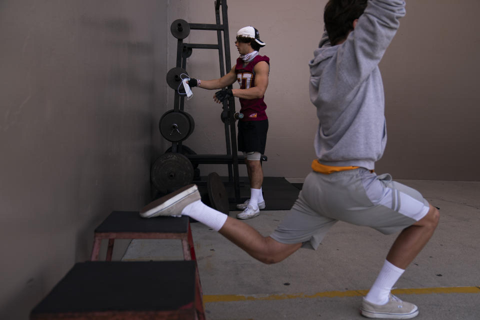 El Modena tight end Owen Mull hangs his mask on a weight bar while working out at a school gym temporarily set up at outdoor racquetball courts before the team's high school football game with El Dorado in Orange, Calif., Friday, March 19, 2021. (AP Photo/Jae C. Hong)