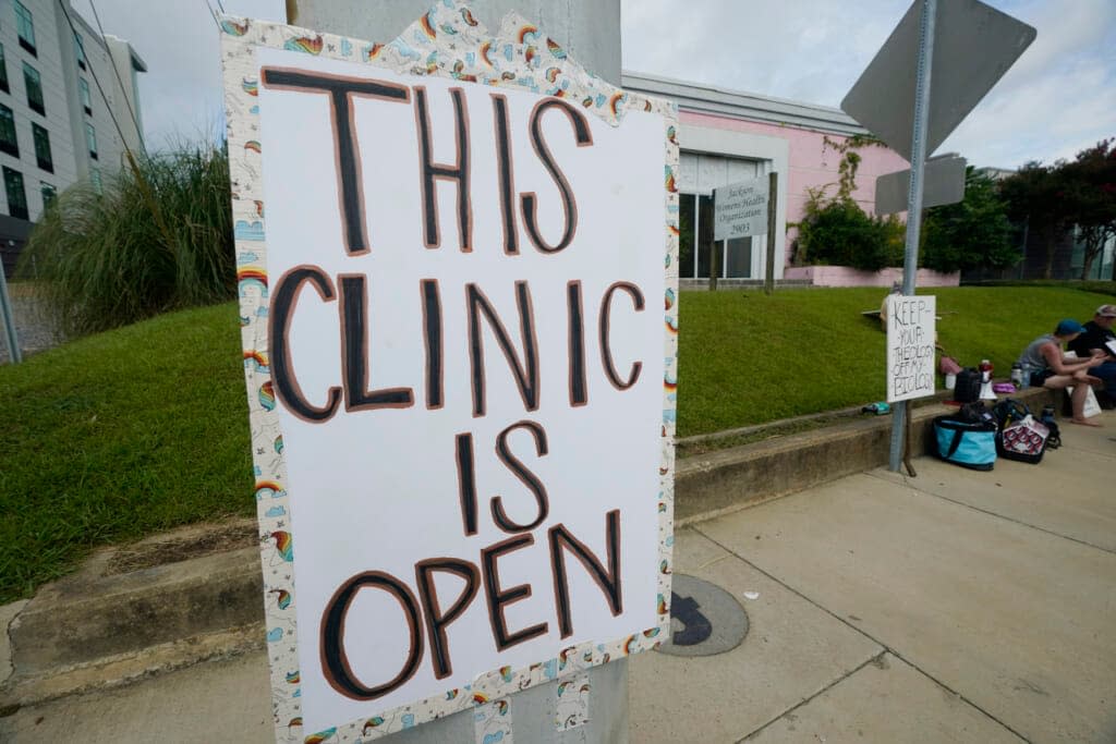 A posted sign outside the Jackson Women’s Health Organization clinic on Sunday, July 3, 2022 assures potential patients that it is open. The clinic, located in Jackson, Miss., is the only facility in the state that performs abortions. (AP Photo/Rogelio V. Solis)