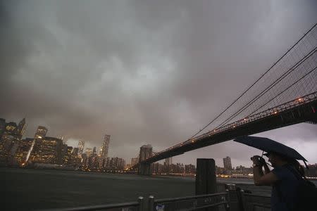 A man stands underneath the Brooklyn Bridge to photograph a summer storm bearing down on New York July 2, 2014. REUTERS/Lucas Jackson