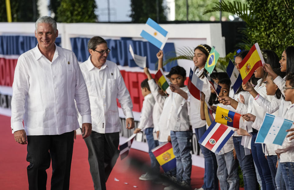 El presidente de Cuba, Miguel Díaz-Canel, a la izquierda, acompañado por el ministro de Relaciones Exteriores de Cuba, Bruno Rodríguez, camina junto a algunos niños que ondean banderas a su llegada a la sesión de la 28ª Cumbre Iberoamericana, en Santo Domingo, República Dominicana, el sábado 25 de marzo de 2022. (Foto AP/Ariana Cubillos)