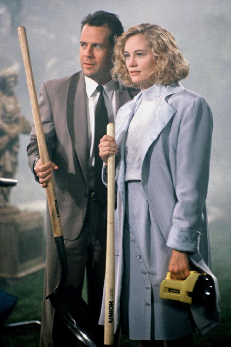 A man in a suit and a woman in a pale blue skirt suit, both holding large wooden sticks