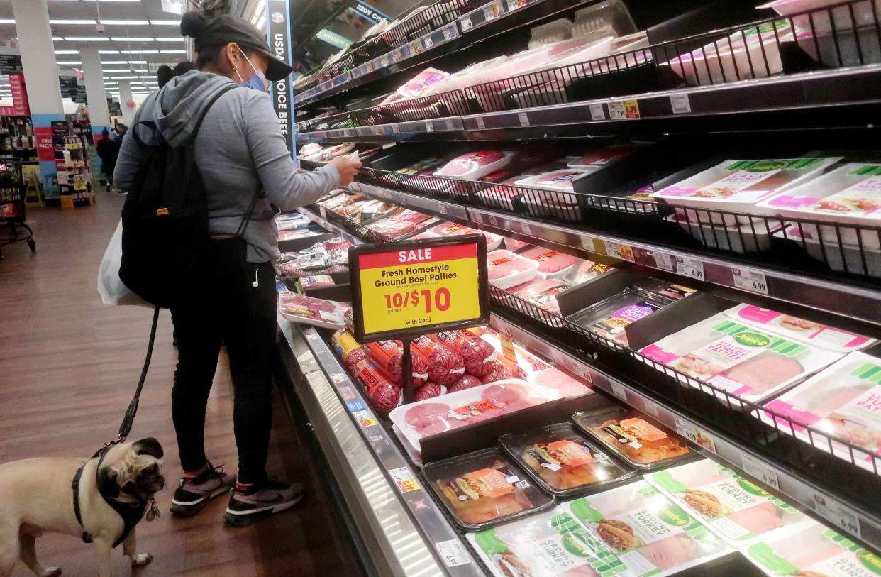 A person shops for beef in a supermarket with a pug on a leash.