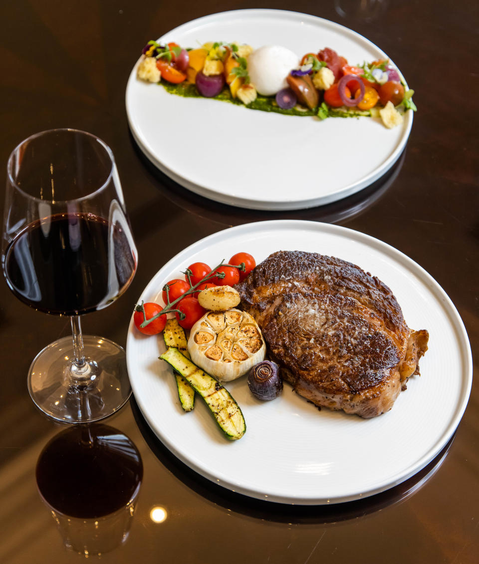 At Stirrups Restaurant, a glass of red wine is served with this 16-ounce grilled ribeye and heirloom tomato salad. The steak is garnished with a grilled clove of garlic along with other vegetables.