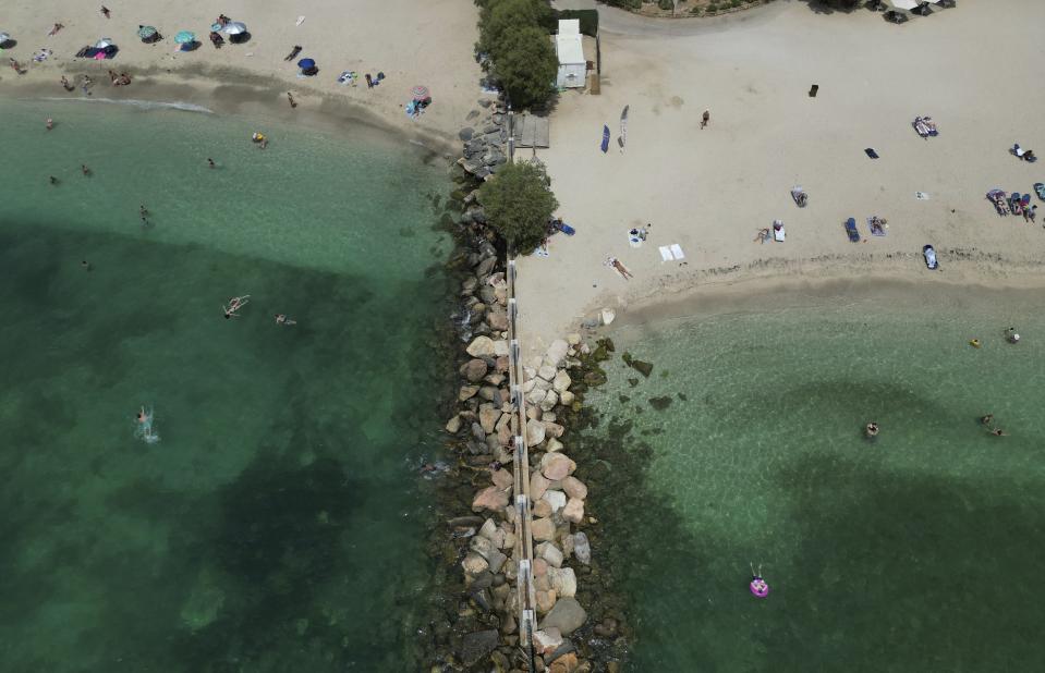 People enjoy the sea and the beach in southern Athens, Greece, on Wednesday, July 26, 2023. A third successive heat has struck Greece, with the temperature in many parts of the country soaring Wednesday to as high as 46.4C (115 Fahrenheit), while many wildfires raged out of control for days in the country. (AP Photo/Thanassis Stavrakis)