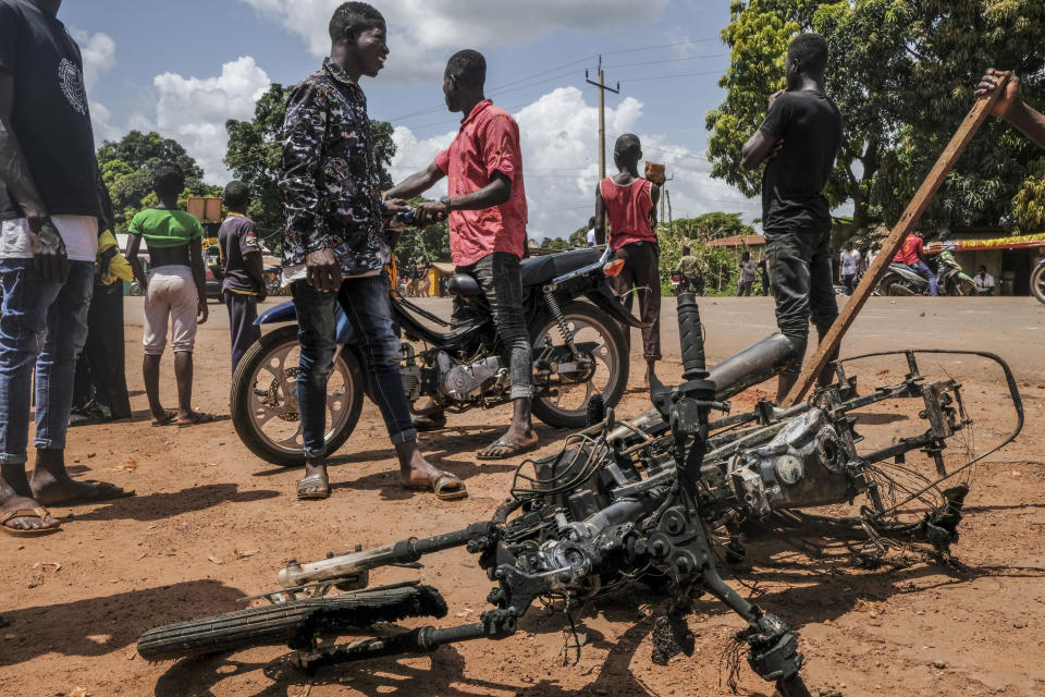 The burned motorcycle of an opposition activist, who was lightly injured and fled, lies on the ground as supporters of the ruling Rally of the Guinean People (RPG) party demonstrate against the opposition Union of Democratic Forces of Guinea (UFDG) party and to block the visit of their leader, in the streets of Kankan, Guinea Sunday, Oct. 11, 2020. The stage is set for Oct. 18 presidential elections pitting incumbent President Alpha Conde, 82, who is bidding for a third term, against opposition leader Cellou Dalein Diallo, who was previously defeated by Conde in both the 2010 and 2015 elections. (AP Photo/Sadak Souici)