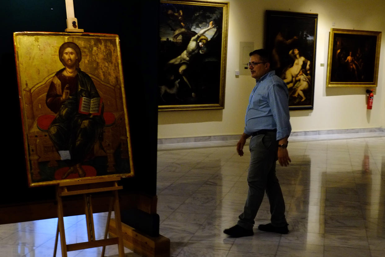 Director of Byzantine museum in Cyprus Ioannis Eliades walks past a looted 500 year-old Orthodox icon of the Enthroned Christ is seen at the Byzantine Museum after it was returned, in capital Nicosia, Cyprus, on Tuesday, July 12, 2022. A 500 year-old Orthodox icon of the Enthroned Christ that was looted from a 12th century church in the breakaway north of ethnically divided Cyprus was repatriated after the end of a years-long legal journey from Zurich, Switzerland. (AP Photo/Petros Karadjias)