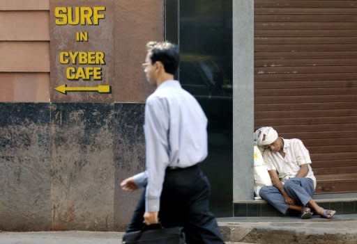 This file photo shows an Indian man passing a Cyber Cafe sign while another one sleeps in a doorway, in Mumbai, in 2004. Global hacking movement Anonymous has called for protesters to take to the streets in 16 cities around India on Saturday over what it considers growing government censorship of the Internet