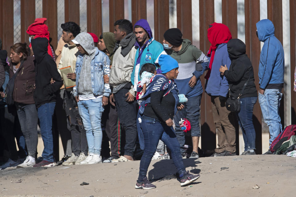 ARCHIVO - Una mujer migrante carga a un niño en su espalda mientras observa la línea de otros migrantes que tratan de ingresar a El Paso, Texas, luego de cruzar el Río Bravo desde Ciudad Juárez, México, el 21 de diciembre de 2022. (AP Foto/Andres Leighton, archivo)