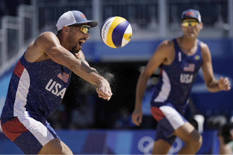 Nicholas Lucena, left, of the United States, returns a shot as teammate Philip Dalhausser watches during a men's beach volleyball match against Qatar at the 2020 Summer Olympics, Sunday, Aug. 1, 2021, in Tokyo, Japan. (AP Photo/Felipe Dana)