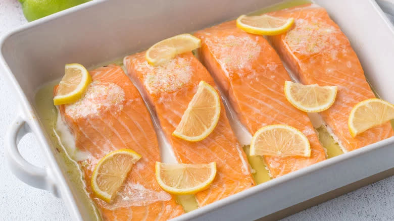 Raw salmon fillets with lemon slices in dish