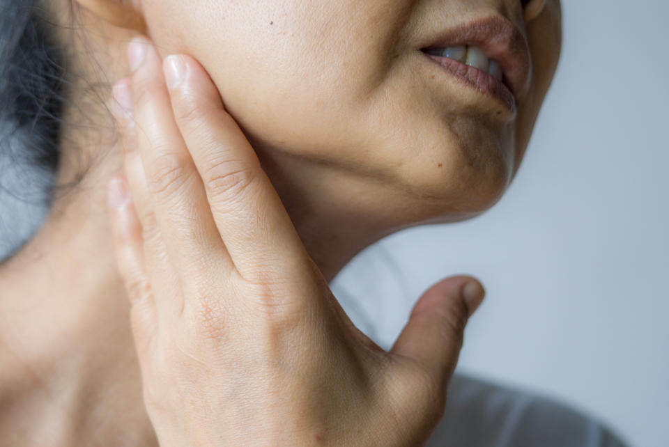 A woman feeling pain, holding her jaw with hand, suffering from bad tooth ache.