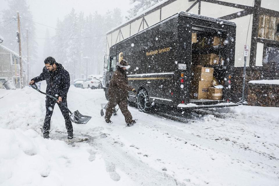 A man shovels snow near a delivery truck.