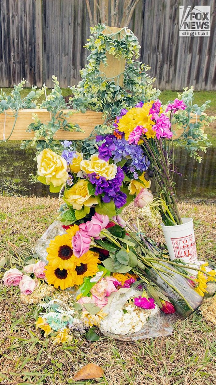 A small wooden cross covered with flowers by the side of a highway