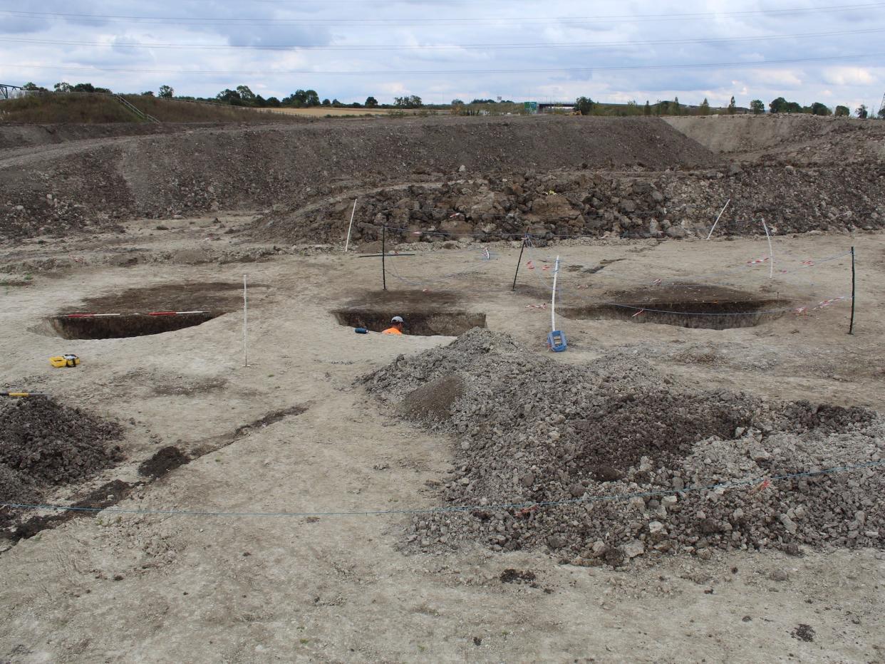 Three Mesolithic-period pits in alignment in Bedfordshire, England being excavated by an archaeologist in an orange jumpsuit