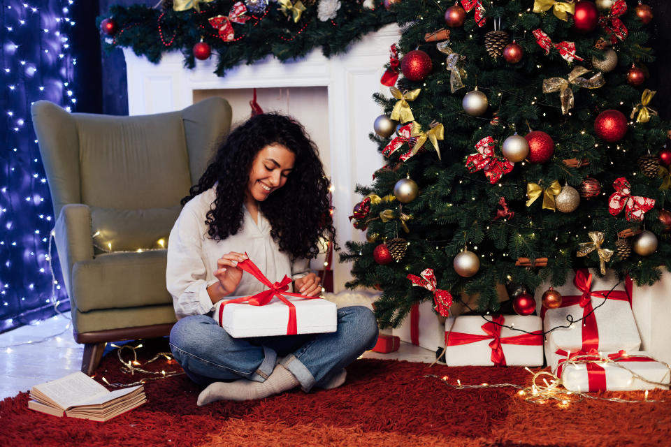 brunette woman opens presents at Christmas tree with lights garlands new year