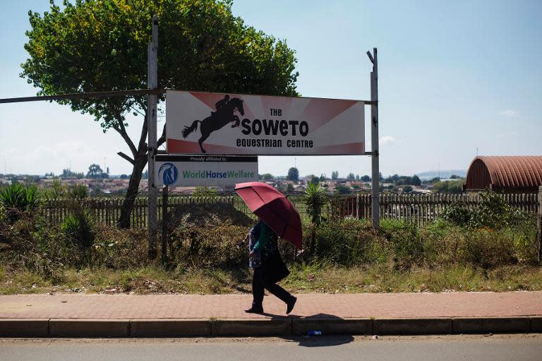 A Soweto resident protects herself from the sun with an umbrella as she walks in front of the Soweto Equestrian Center on April 15, 2014