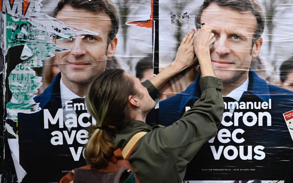 A protester damages a campaign poster bearing French President and candidate for a second term Emmanuel Macron during a "Look up" march, to call on the presidential candidates to take into account the climate emergency, which protesters say is largely absent from the election campaign, less than two weeks after a warning from UN climate experts and a month before the presidential election, in Rennes, western France, on March 12, 2022 - DAMIEN MEYER/AFP