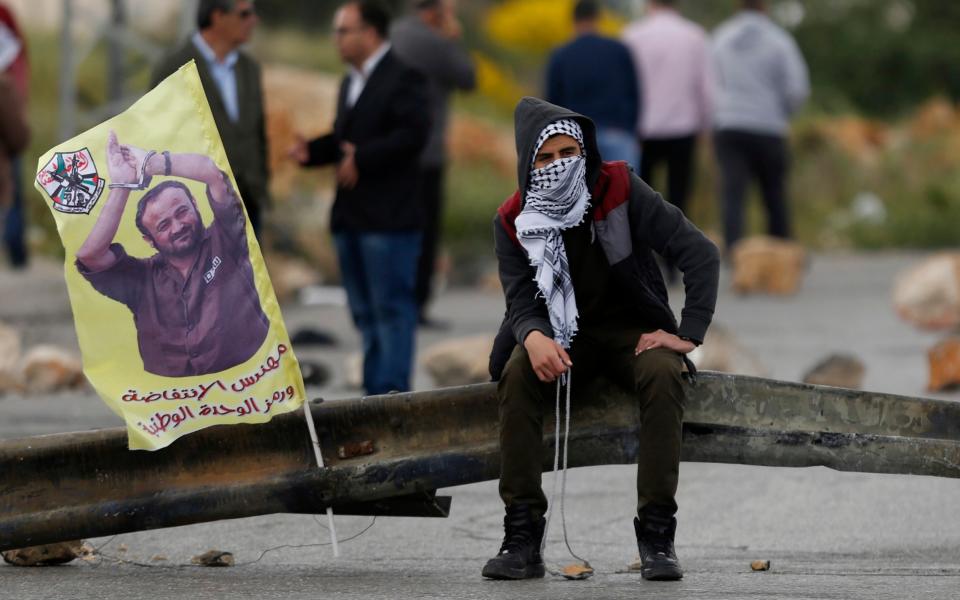 A Palestinian protester holds a sling shot as he sits near a banner with a picture of jailed leader Marwan Barghouti that reads: reads