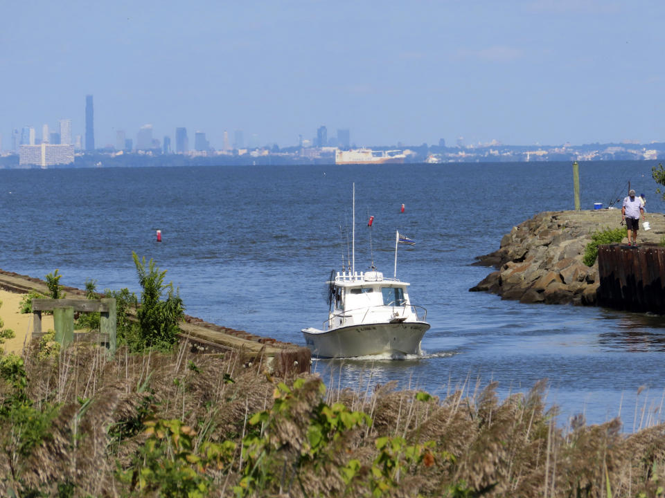 With the New York City skyline in the background, a boat enters a creek on Wednesday, Sept. 20, 2023, in a section of Middletown, N.J., that was hit hard by Superstorm Sandy. New Jersey, like places around the world, is setting ambitious goals to deal with climate change, but it wrestling with how much to actually require of businesses and individuals to fulfill those goals. (AP Photo/Wayne Parry)