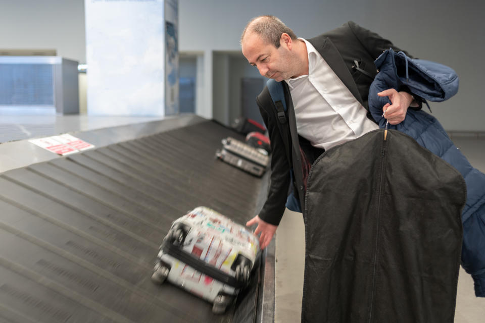 Man in a suit reaching for luggage on an airport conveyor belt