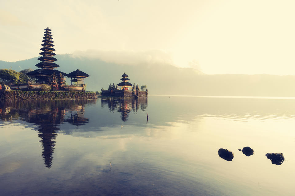 Sunrise over a Balinese floating temple on lake Bratan with misty mountains in the background