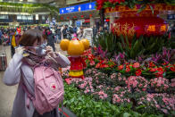 A traveler adjusts her face mask next to a display for the upcoming Lunar New Year at the Beijing West Railway Station in Beijing, Tuesday, Jan. 21, 2020. A fourth person has died in an outbreak of a new coronavirus in China, authorities said Tuesday, as more places stepped up medical screening of travelers from the country as it enters its busiest travel period. (AP Photo/Mark Schiefelbein)