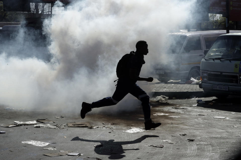 A man runs away from teargas after making off with goods from a store in Germiston, east of Johannesburg, South Africa, Tuesday, Sept. 3, 2019. Police had earlier fired rubber bullets as they struggled to stop looters who targeted businesses as unrest broke out in several spots in and around the city. (AP Photo/Themba Hadebe)