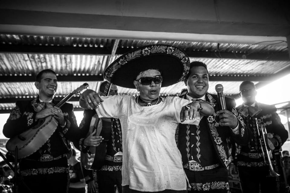 A woman sings in front of a band of Mariachis.