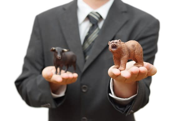 Person in a suit holding a toy bear in one hand and a toy bull in the other.