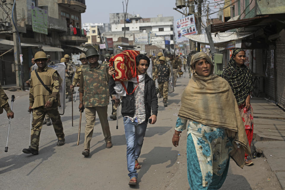 An Indian Muslim family leaves the area as Indian paramilitary soldiers patrol a street vandalized in Tuesday's violence in New Delhi, India, Thursday, Feb. 27, 2020. India accused a U.S. government commission of politicizing communal violence in New Delhi that killed at least 30 people and injured more than 200 as President Donald Trump was visiting the country. The violent clashes between Hindu and Muslim mobs were the capital's worst communal riots in decades and saw shops, Muslim shrines and public vehicles go up in flames. (AP Photo/Altaf Qadri)