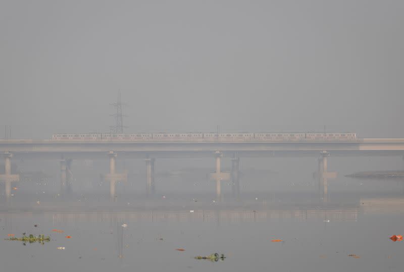 A metro train moves over a bridge built over the Yamuna river on a smoggy morning in the old quarters of Delhi