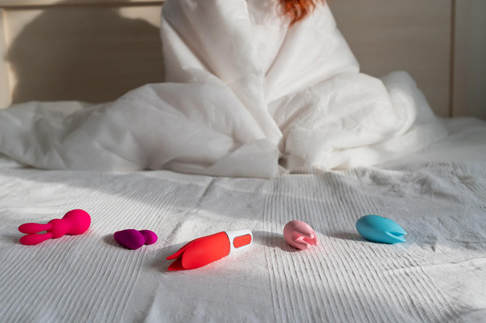 woman on bed with collection of sex toys