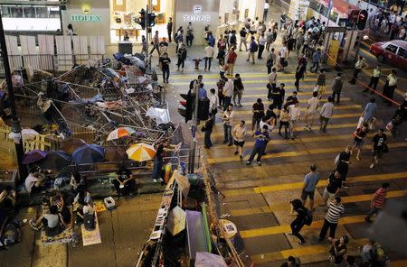Pedestrians walk by a barricade as pro-democracy protesters block a street at the Mongkok shopping district of Hong Kong October 19, 2014. REUTERS/Carlos Barria