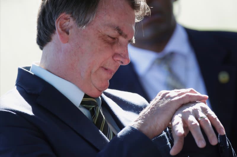 Brazil's President Jair Bolsonaro looks at his watch while meeting supporters as he leaves at Alvorada Palace, amid coronavirus disease (COVID-19) outbreak, in Brasilia