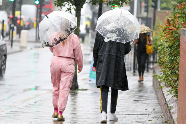 People sheltering from the rain beneath umbrellas walk past a