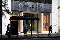 CORRECTS YEAR TO 2020 NOT 2019 Two pedestrians wait for a bus as another runs past the Italian luxury store Bulgari, known for its jewelry, watches, fragrances, accessories and leather goods, on Chicago's Magnificent Mile on Tuesday, Aug. 11, 2020. Store owners in and around Chicago's Michigan Avenue are asking themselves if of the economics and reputation of one America’s most prestigious shopping districts can rebound from the damage caused by looting this week. Businesses had been slowly reopening after pandemic-related shutdowns. (AP Photo/Charles Rex Arbogast)