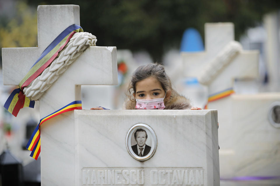 A child, wearing a mask for protection against the COVID-19 infection, leans on the cross of a 1989 anti-communist revolution victim after a memorial religious service for those killed in the uprising, in Bucharest, Romania, Monday, Dec. 21, 2020. Participants and relatives of those killed marked the anniversary of the anti-communist uprising which started in Bucharest on Dec. 21, 1989, left more than one thousand people dead and ended the rule of dictator Nicolae Ceausescu. (AP Photo/Vadim Ghirda)