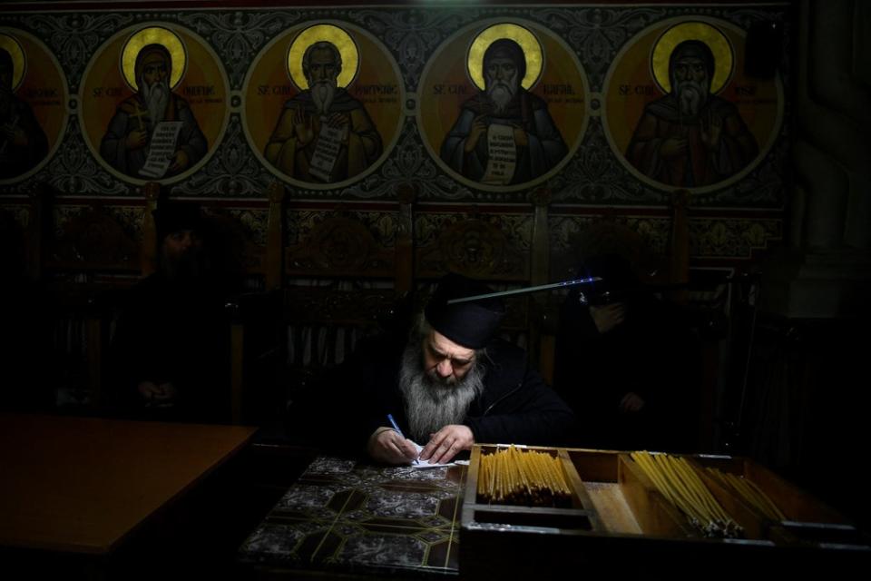 Father Caliopie takes lists of names of the dead and writes allocated prayer times for them, before service begins in the church at Putna monastery (Reuters)