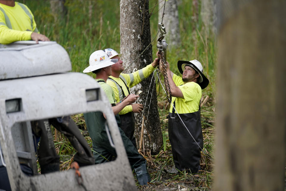 Electrical workers install guy wires for a new utility pole in a marsh in the aftermath of Hurricane Ida in Houma, La., Friday, Sept. 17, 2021. The Louisiana terrain presents special challenges. In some areas, lines thread through thick swamps that can be accessed only by air boat or marsh buggy, which looks like a cross between a tank and a pontoon boat. Workers don waders to climb into muddy, chest-high waters home to alligators and water moccasins. (AP Photo/Gerald Herbert)