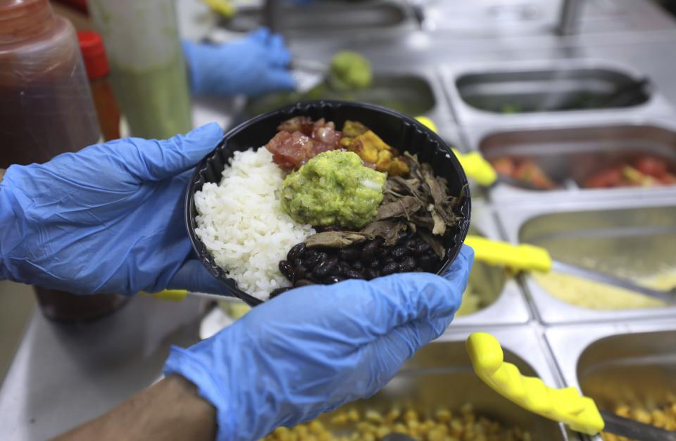 An employees holds a food order at a MUY restaurant, a Colombian fast food chain that is planning to turn its branches into automated restaurants, in Bogota, Colombia, Thursday, Aug. 13, 2020. The chain has opened its first “contactless store” in a commercial district of Bogota, where many restaurants have been forced to shut down because of a ban on sit-down dining. (AP Photo/Fernando Vergara)