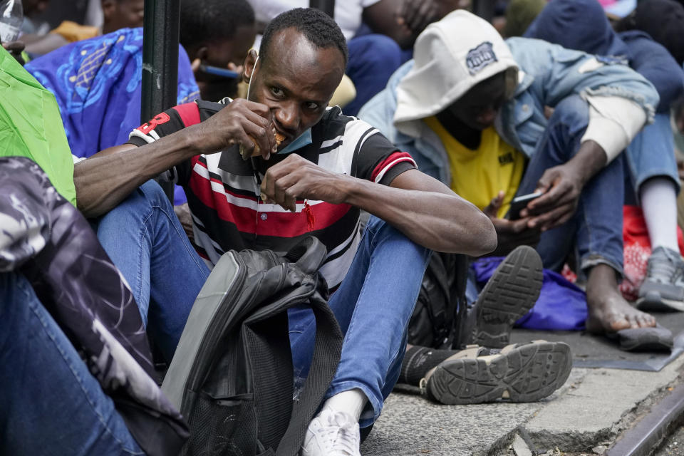 Migrants sit in a queue outside of The Roosevelt Hotel that is being used by the city as temporary housing, Monday, July 31, 2023, in New York. (AP Photo/John Minchillo)