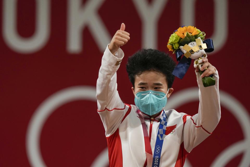 Hou Zhihui of China celebrates on the podium after winning the gold medal in the women's 49kg weightlifting event, at the 2020 Summer Olympics, Saturday, July 24, 2021, in Tokyo, Japan. (AP Photo/Luca Bruno)