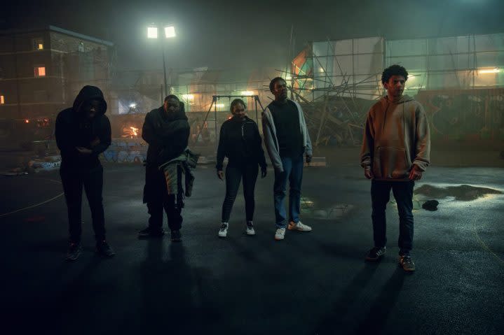 Five people stand in a dark alley and stare.