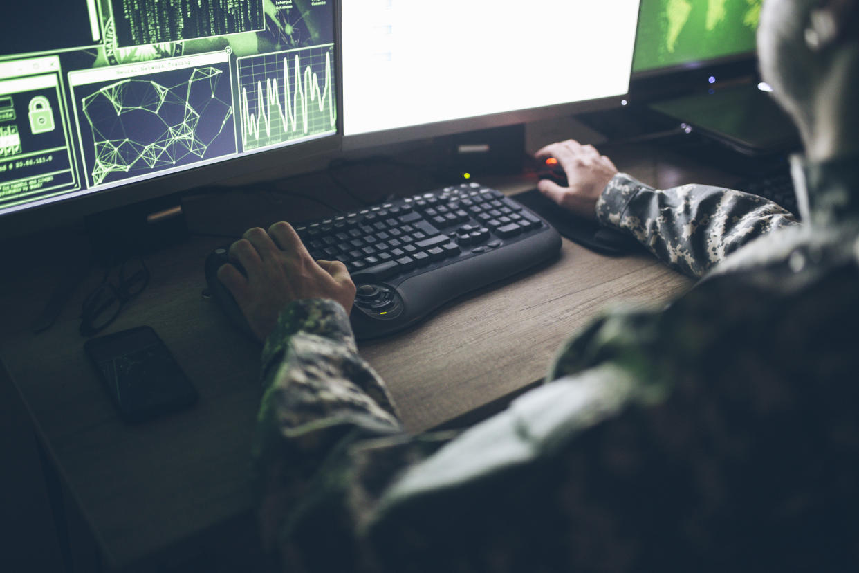 A military service member sitting at a desk and typing on a computer keyboard.