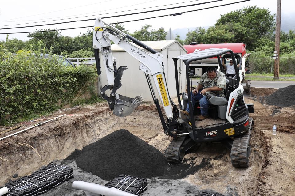 Contractor Wendall Bandmann drives an excavator helping to install a leach field, which is connected to a septic tank, to replace a residential cesspool, Thursday, May 11, 2023, in Waialua, Hawaii. Hawaii has 83,000 of cesspools, more than any other U.S. state, and many of them are close to the shoreline. (AP Photo/Marco Garcia)