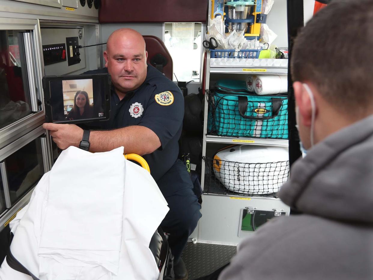 Firefighter/paramedic Adam Lovell, left, holds a tablet showing Dr. Holli Hill via the Akron Fire Department's telehealth program during a demonstration with firefighter/paramedic Dan Hilton portraying the patient in 2021.