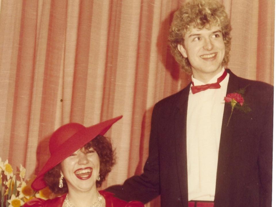 A bride and groom. The bride is wearing a red dress and hat.