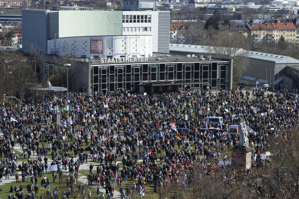 Participants stand in front of the State Theater during a rally taking place under the motto "Free citizens Kassel - basic rights and democracy" in Kassel, Germany, Saturday, March 20, 2021. According to police, several thousand people were on the move in the city center and disregarded the instructions of the authorities during the unregistered demonstration against Corona measures. (Swen Pfoertner/dpa via AP)